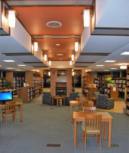 Central hub of new public library in Barneveld Wisconsin features a fireplace, collection shelves and ample tables for visitor use.