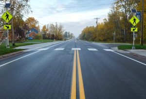 Photograph of a newly rehabilitated roadway along Ugstad Road in Hermantown, Minnesota, with new safer pedestrian crossing and rectangular rapid flashing beacons to alert vehicles.