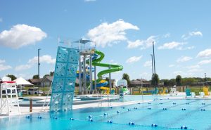 Colorful image, taken poolside at the new aquatic center in Evanvsville, Wisconsin, showing a six-lane swimming pool, aqua climbing wall, lazy river, and waterslide